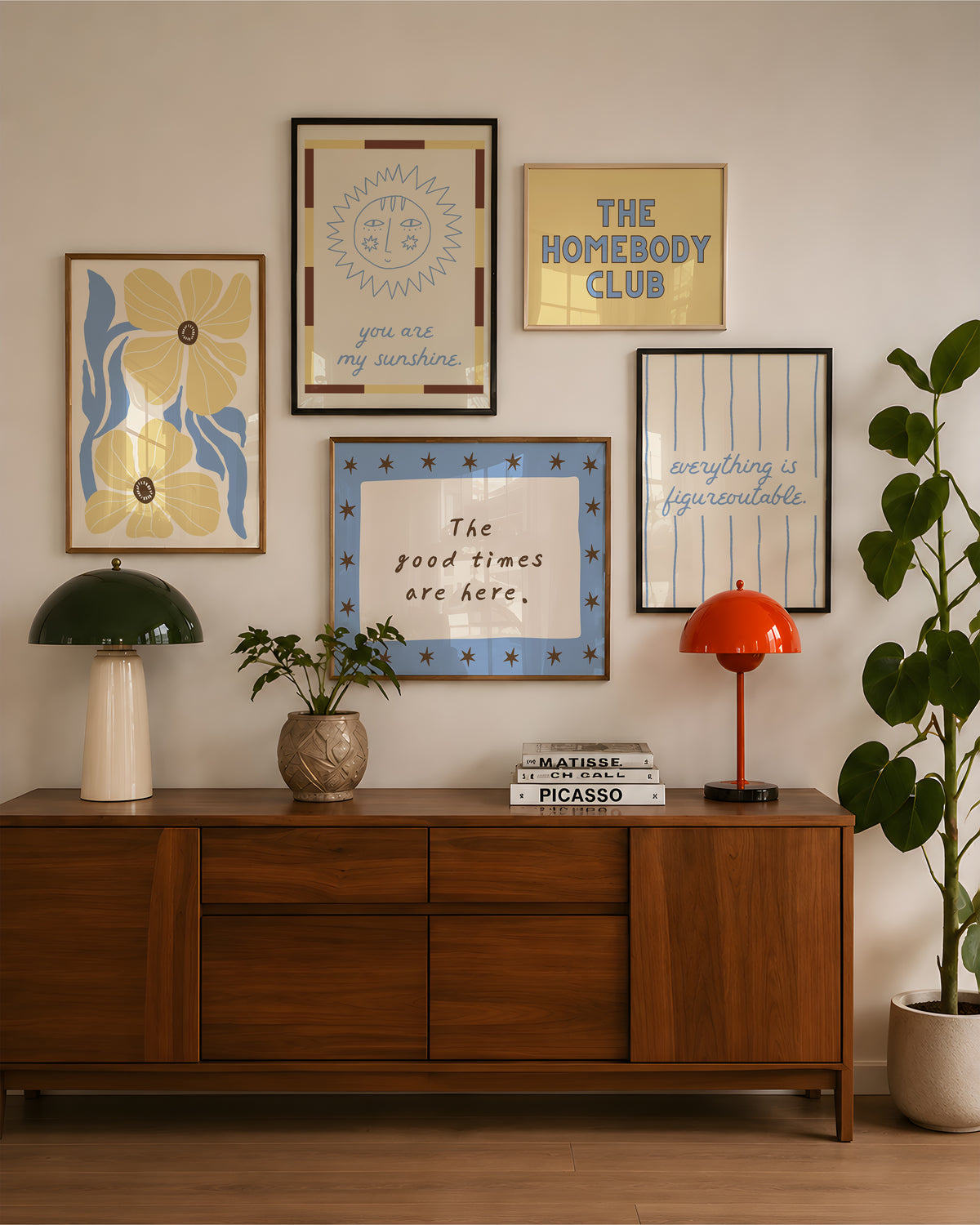 Set of five prints in butter yellow and blue: "The Homebody Club," a floral illustration, "everything is figureoutable," "The good times are here" with stars, and "you are my sunshine" with a sun