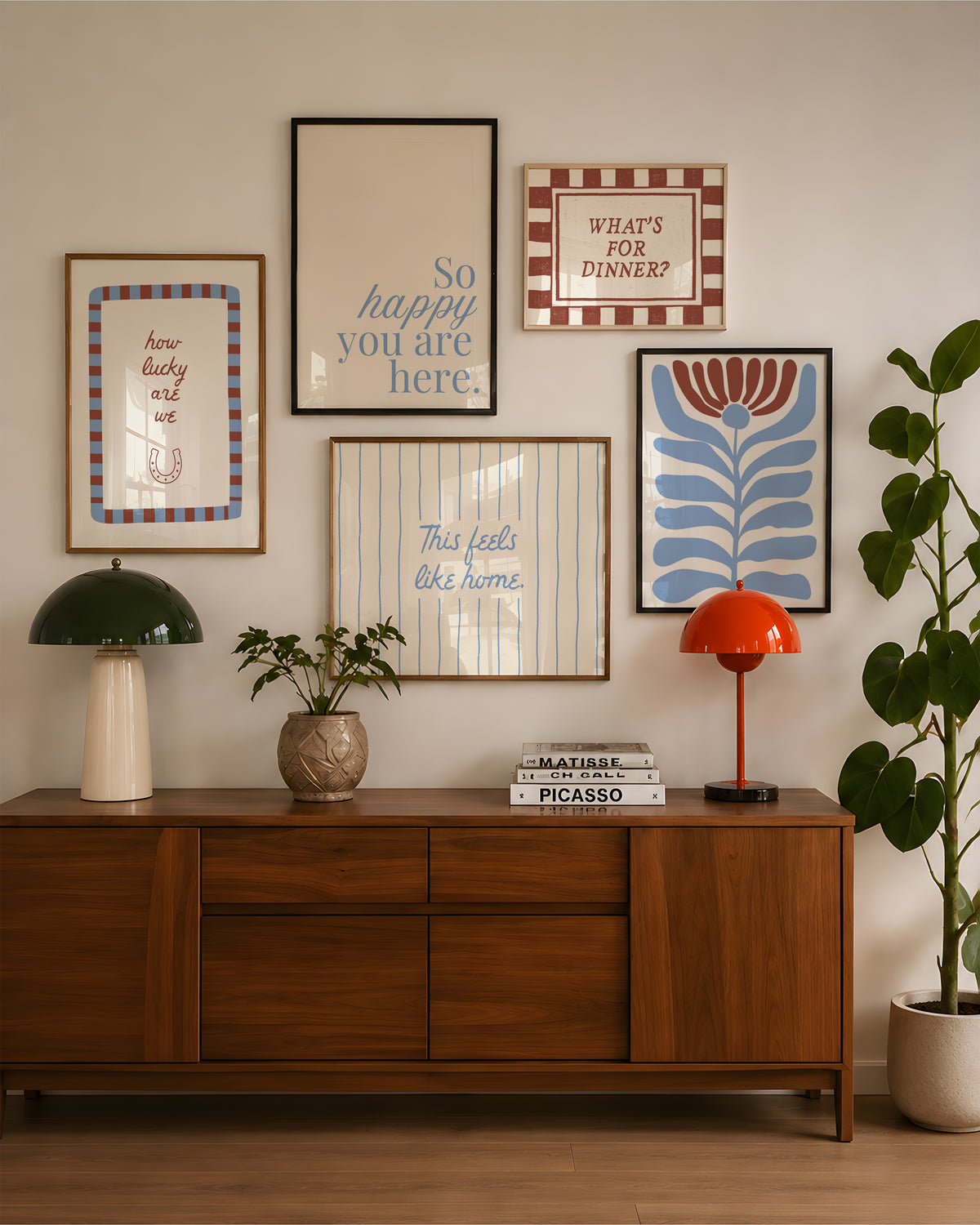 Set of five prints in rust and dusty blue: "How lucky are we" with a horseshoe, "So happy you are here," "What's for dinner?" in a checkered border, "This feels like home" on stripes, and a floral illustration