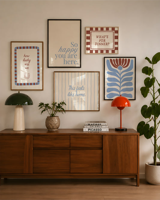 Set of five prints in rust and dusty blue: "How lucky are we" with a horseshoe, "So happy you are here," "What's for dinner?" in a checkered border, "This feels like home" on stripes, and a floral illustration