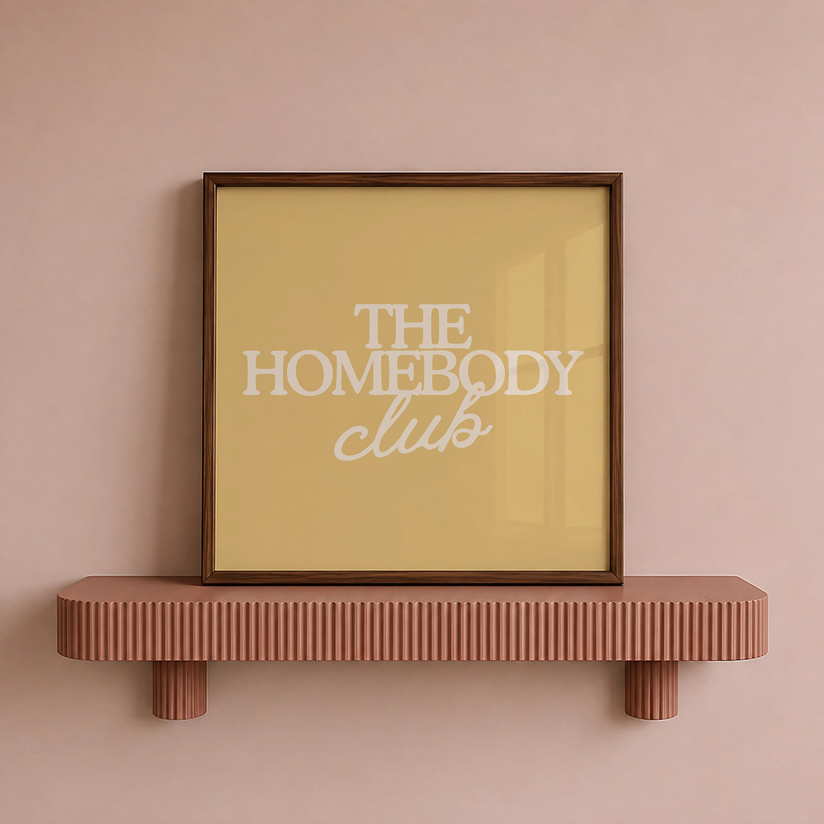 Square digital print with a mustard yellow background featuring "THE HOMEBODY" in bold cream serif type stacked above "club" in cream cursive script, centered typography layout.