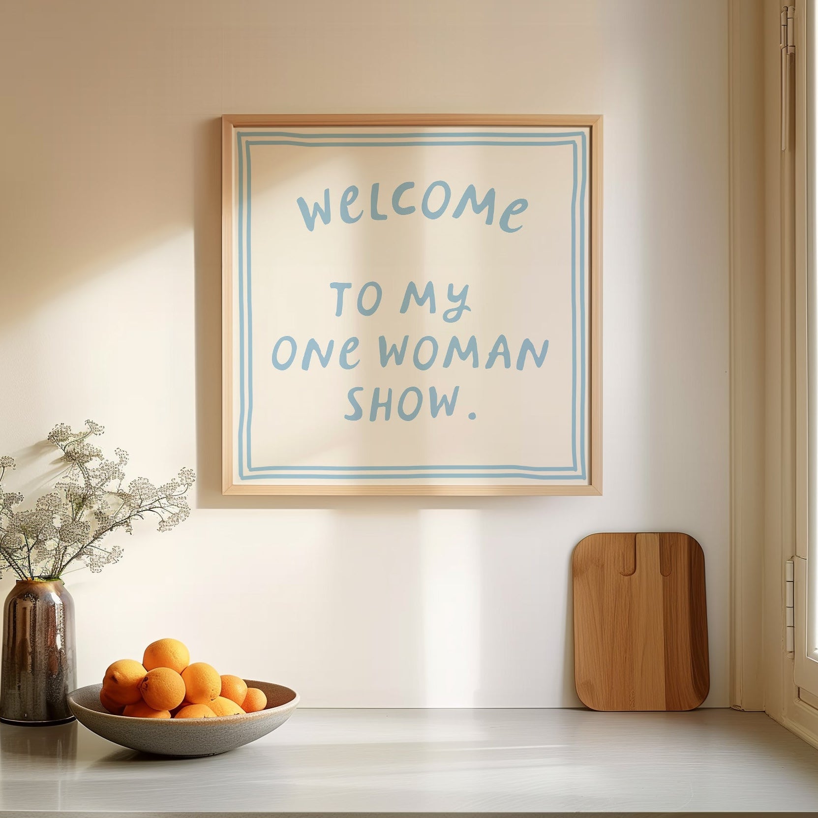 Beige print with dusty blue hand-lettered text "Welcome to my one woman show." inside a double-line border