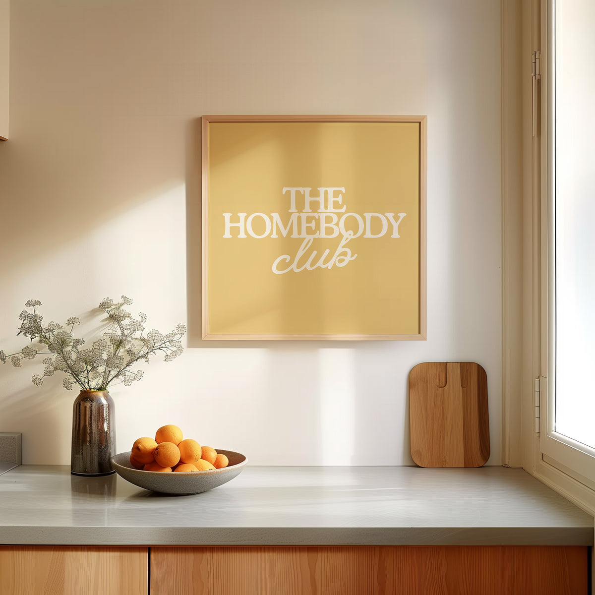 Square digital print with a mustard yellow background featuring "THE HOMEBODY" in bold cream serif type stacked above "club" in cream cursive script, centered typography layout.