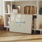 Horizontal print with thin hand-painted tan and cream vertical stripes, the quote "stay awhile" in navy cursive script, and a small hand-drawn smiley face beneath it.