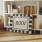 Horizontal print with a bold black and white checkered border framing the word "BOO!" in black hand-drawn type on a textured cream background.