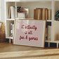 Horizontal wall print with a soft pink centre panel and white border with dark red scalloped outline, bold dark red cursive script reading it actually is all fun & games
