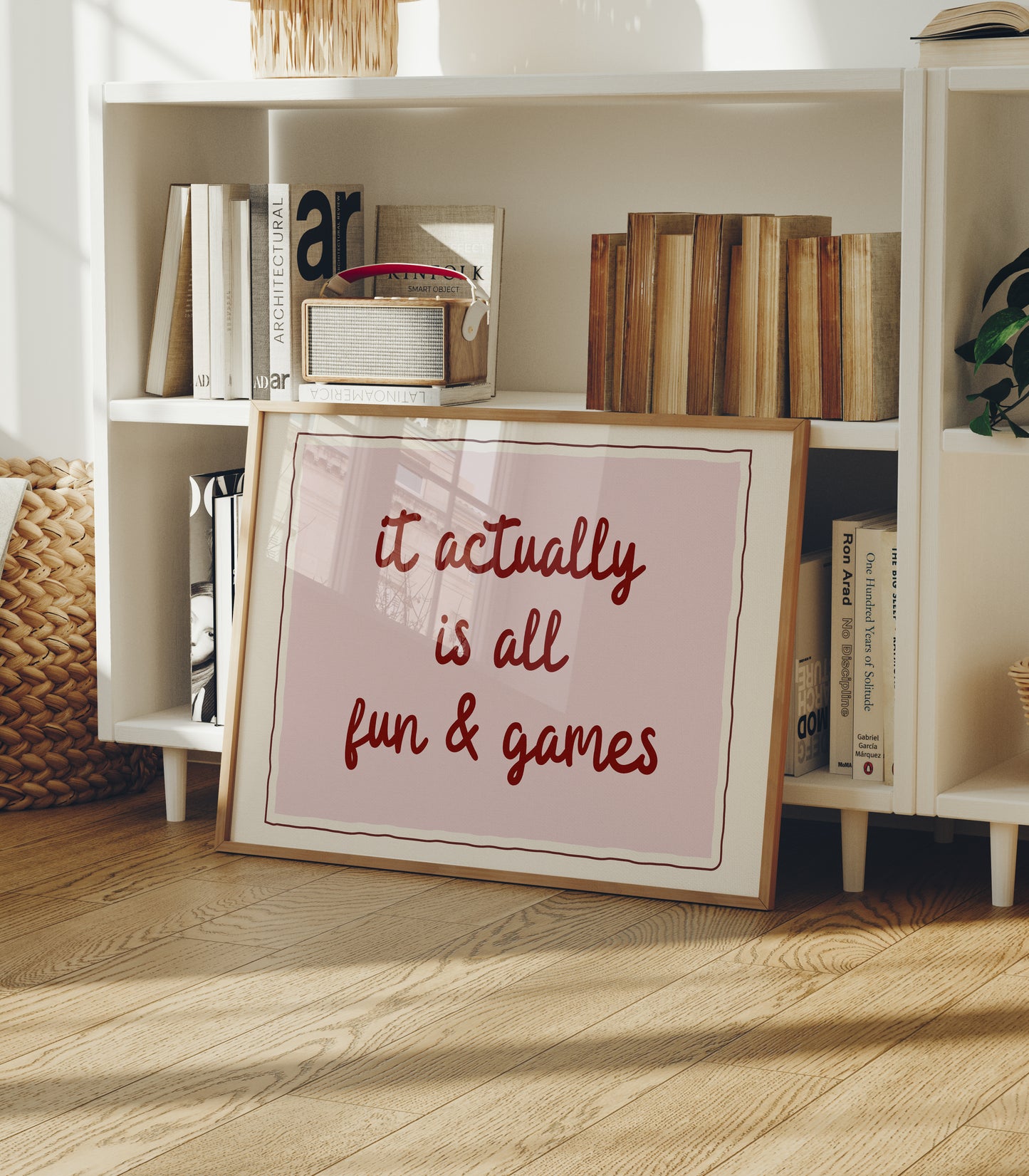 Horizontal wall print with a soft pink centre panel and white border with dark red scalloped outline, bold dark red cursive script reading it actually is all fun & games
