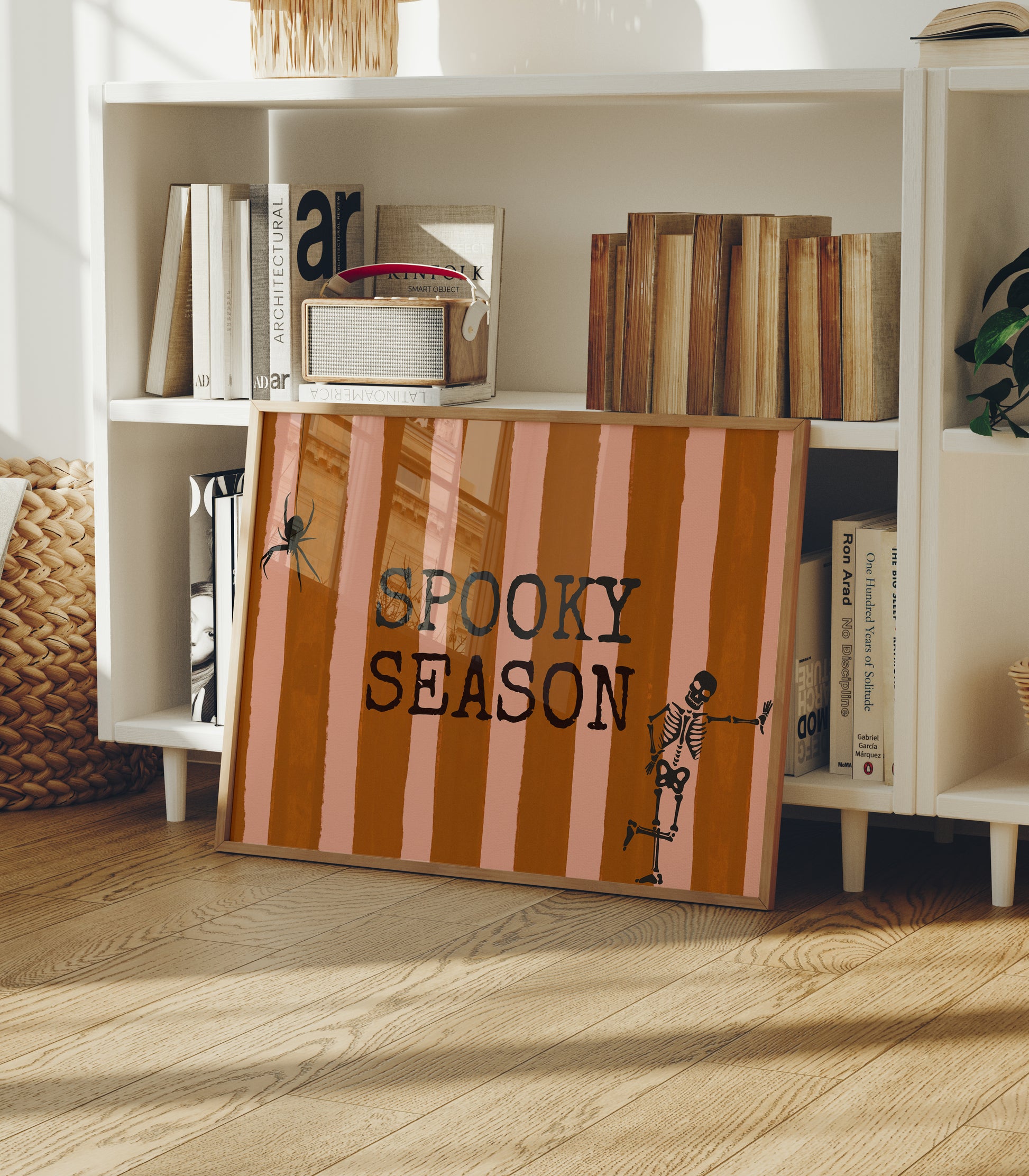 Horizontal print with orange and pink hand-painted vertical stripes, the words "SPOOKY SEASON" in bold black typewriter-style letters, a hanging black spider on the left, and a dancing skeleton illustration on the right.