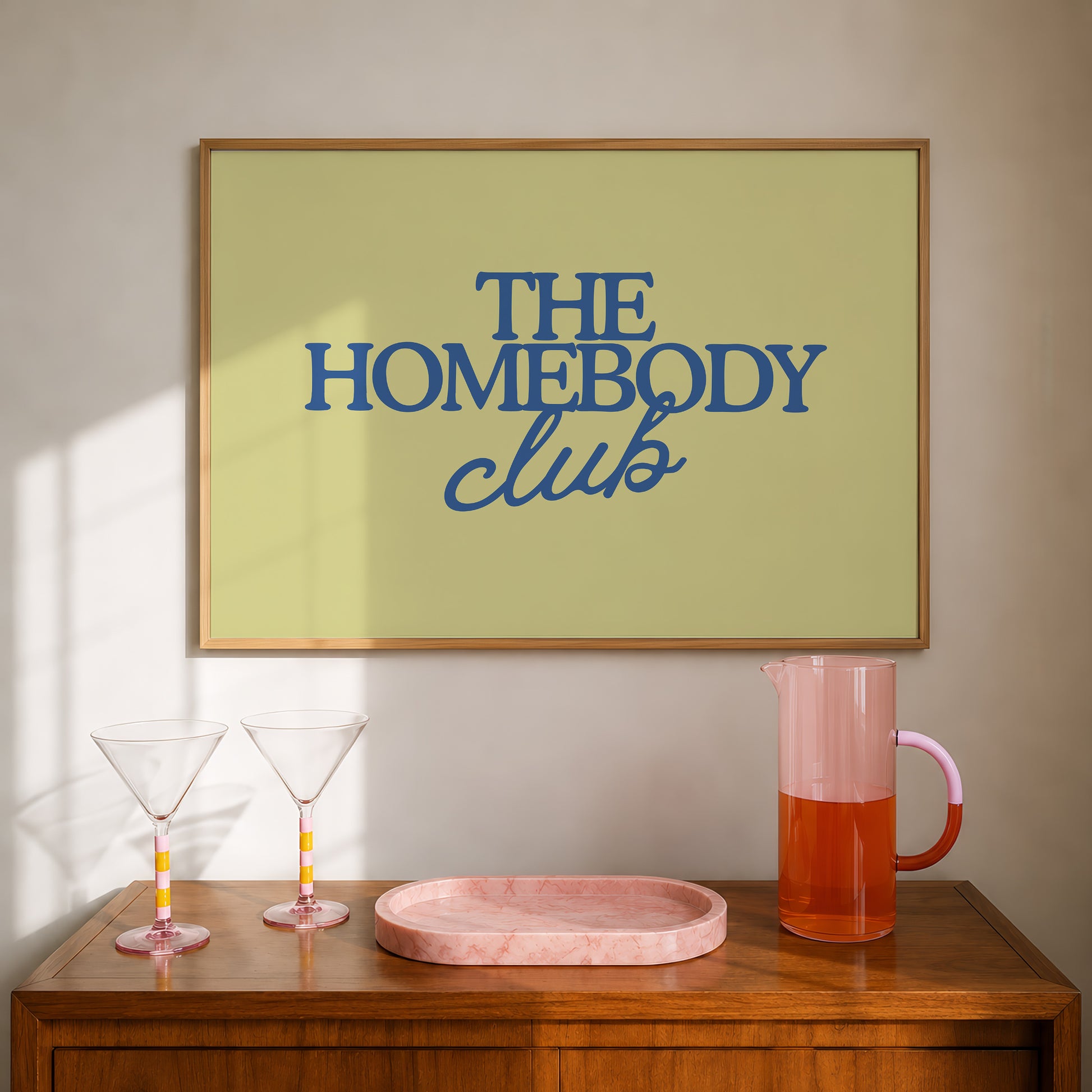 Rectangular landscape digital print with an olive-green background featuring "THE HOMEBODY" in bold blue serif type stacked above "club" in blue cursive script, centered typography layout.