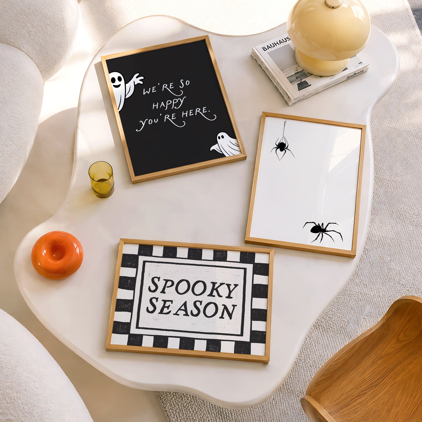 Set of 3 Halloween prints: a black background print with cartoon ghosts reading "We're so happy you're here," a checkered "Spooky Season" print, and a minimalist black spider illustration on a cream background.