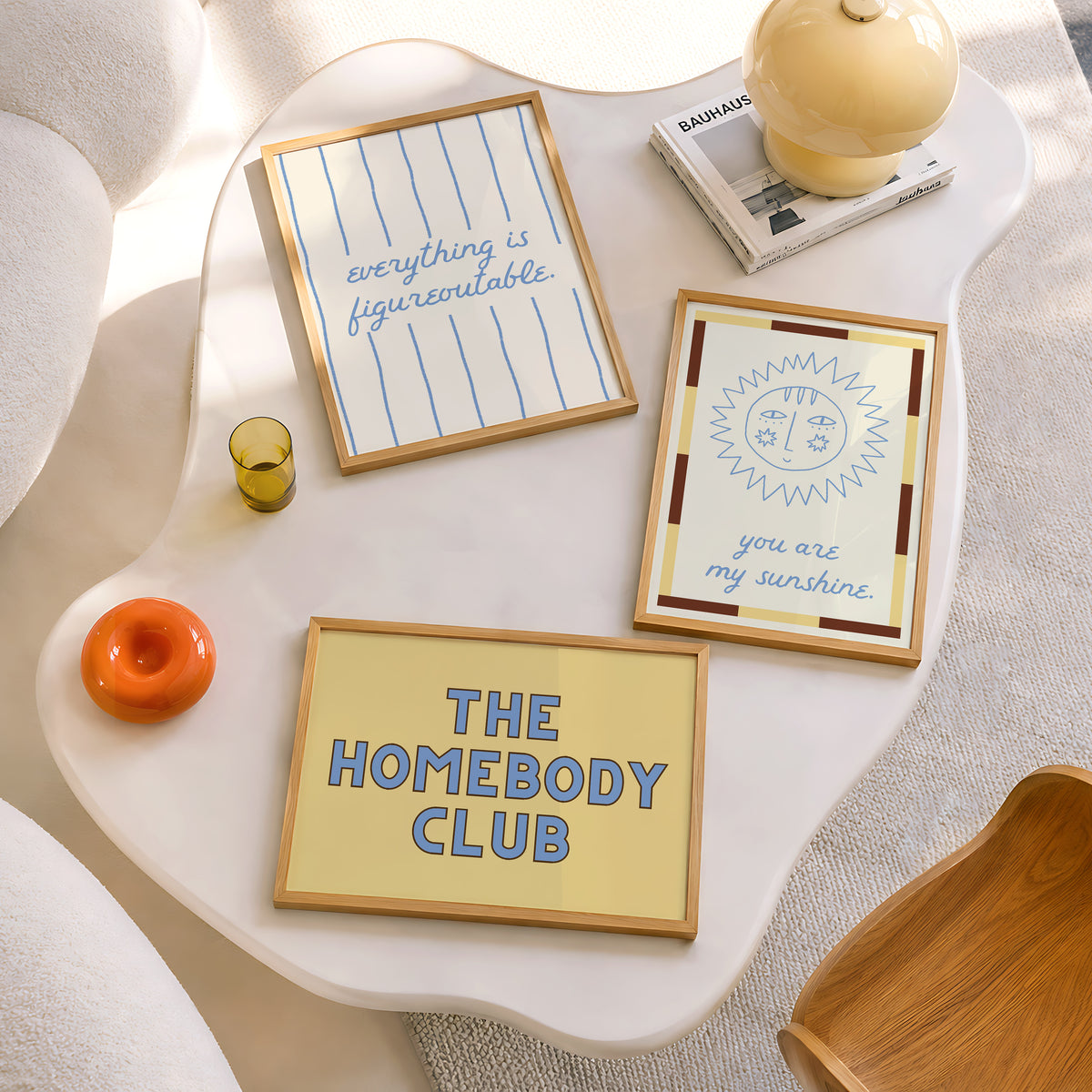Set of five prints in butter yellow and blue: "The Homebody Club," a floral illustration, "everything is figureoutable," "The good times are here" with stars, and "you are my sunshine" with a sun