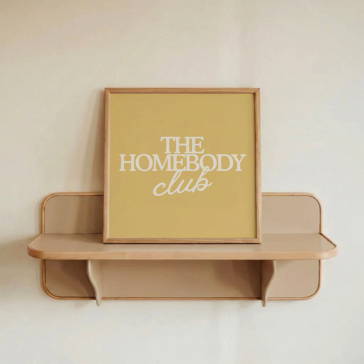 Square digital print with a mustard yellow background featuring "THE HOMEBODY" in bold cream serif type stacked above "club" in cream cursive script, centered typography layout.