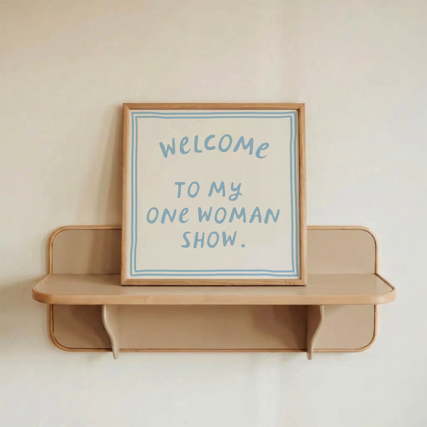 Beige print with dusty blue hand-lettered text "Welcome to my one woman show." inside a double-line border