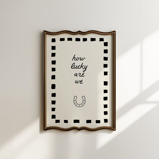 Cream print with a black dashed border featuring the handwritten quote 'how lucky are we' and a horseshoe illustration
