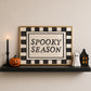 Set of 3 Halloween prints: a black background print with cartoon ghosts reading "We're so happy you're here," a checkered "Spooky Season" print, and a minimalist black spider illustration on a cream background.