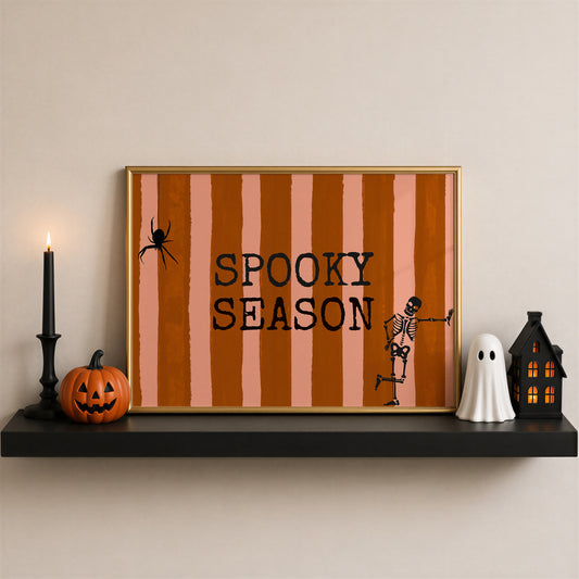 Horizontal print with orange and pink hand-painted vertical stripes, the words "SPOOKY SEASON" in bold black typewriter-style letters, a hanging black spider on the left, and a dancing skeleton illustration on the right.
