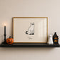 Horizontal minimalist print of a black cat wearing a white ghost sheet costume with cut-out eyes, sitting beside the handwritten word "Boo." on a cream background.