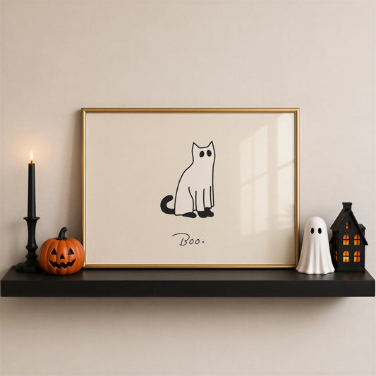Horizontal minimalist print of a black cat wearing a white ghost sheet costume with cut-out eyes, sitting beside the handwritten word "Boo." on a cream background.