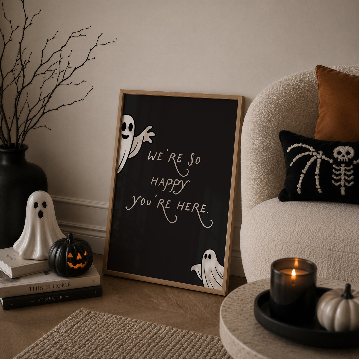 Set of 3 Halloween prints: a black background print with cartoon ghosts reading "We're so happy you're here," a checkered "Spooky Season" print, and a minimalist black spider illustration on a cream background.