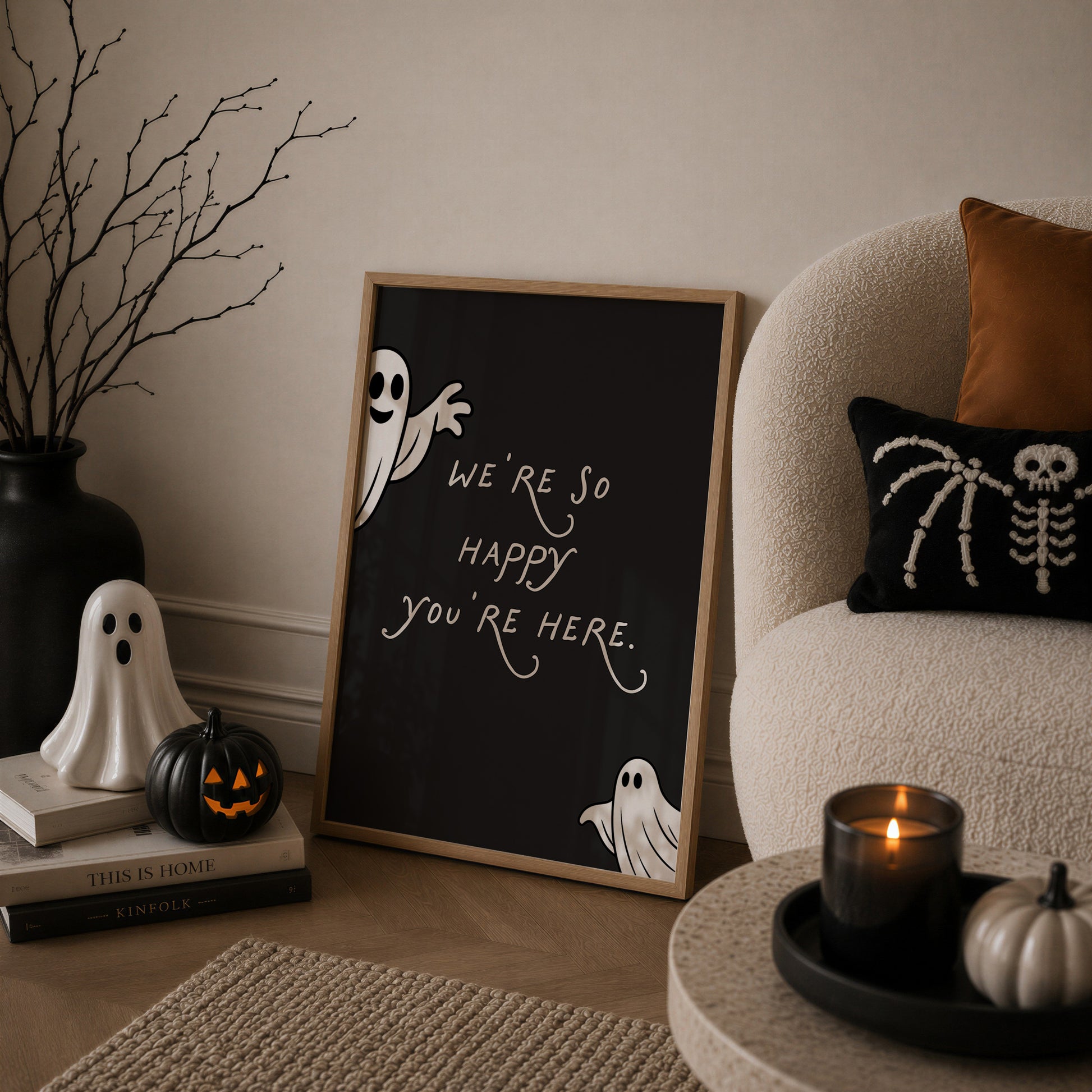 Set of 3 Halloween prints: a black background print with cartoon ghosts reading "We're so happy you're here," a checkered "Spooky Season" print, and a minimalist black spider illustration on a cream background.