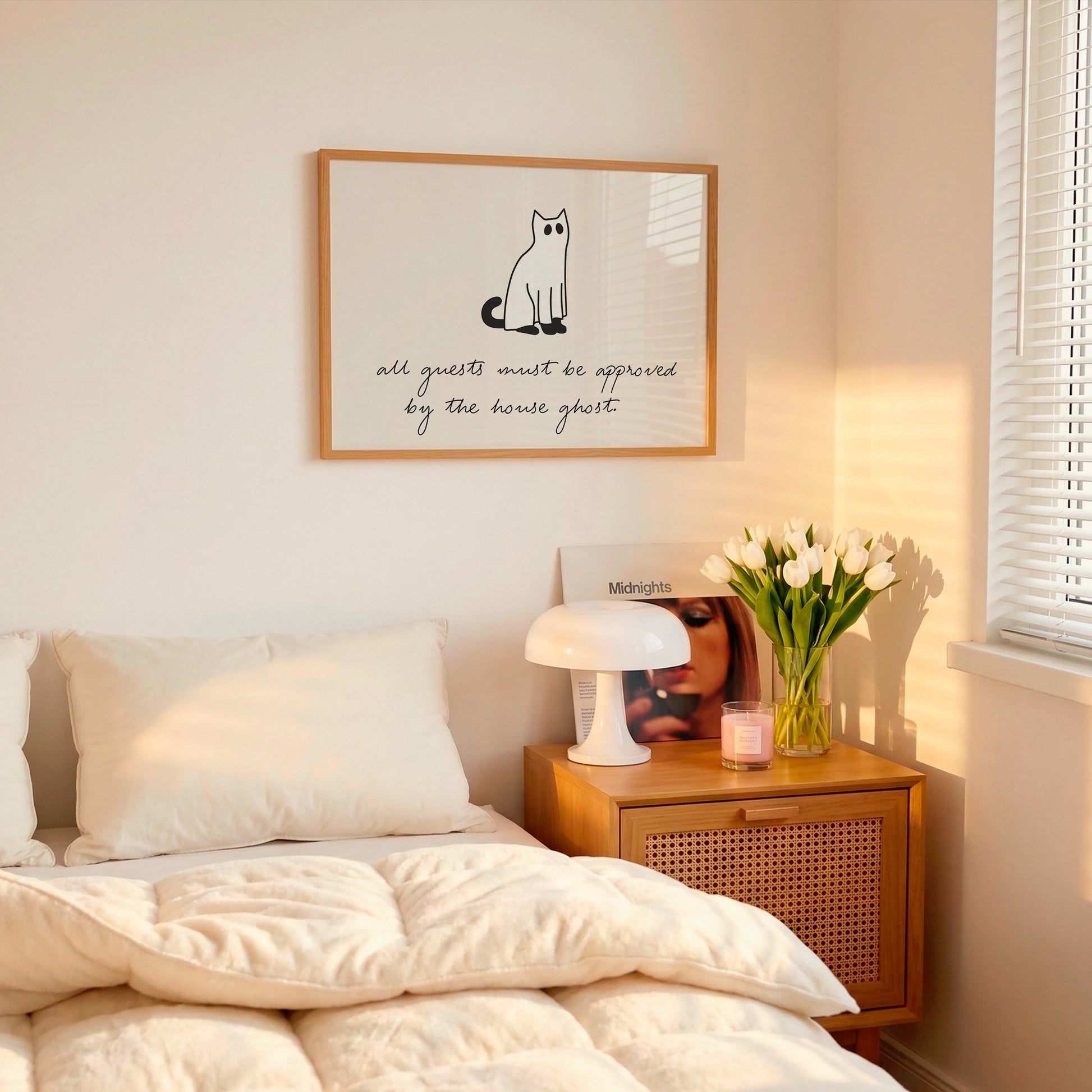 Horizontal minimalist Halloween print of a black cat wearing a white ghost sheet costume with cut-out eyes, above the handwritten cursive quote "all guests must be approved by the house ghost." on a cream background.