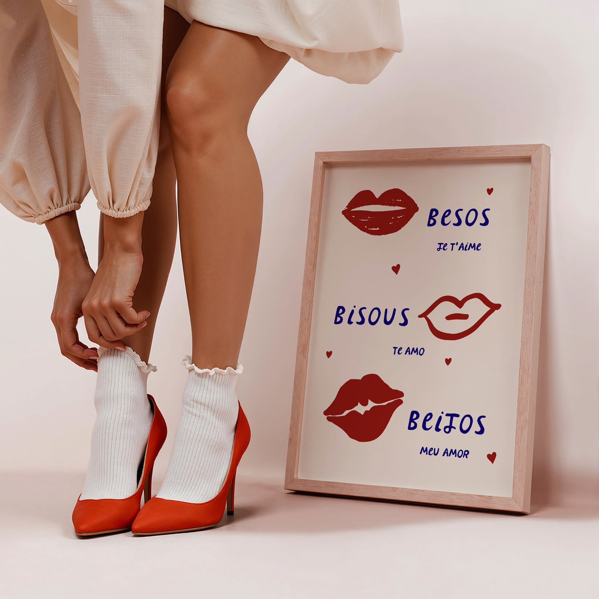 Cream print with three illustrated red lips paired with "Besos," "Bisous," and "Beijos" in navy lettering, with small red hearts scattered throughout