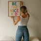 Vertical print with the words "BE THE NICE KID" stacked in large multicolored bubble letters on a cream background in a blue frame.