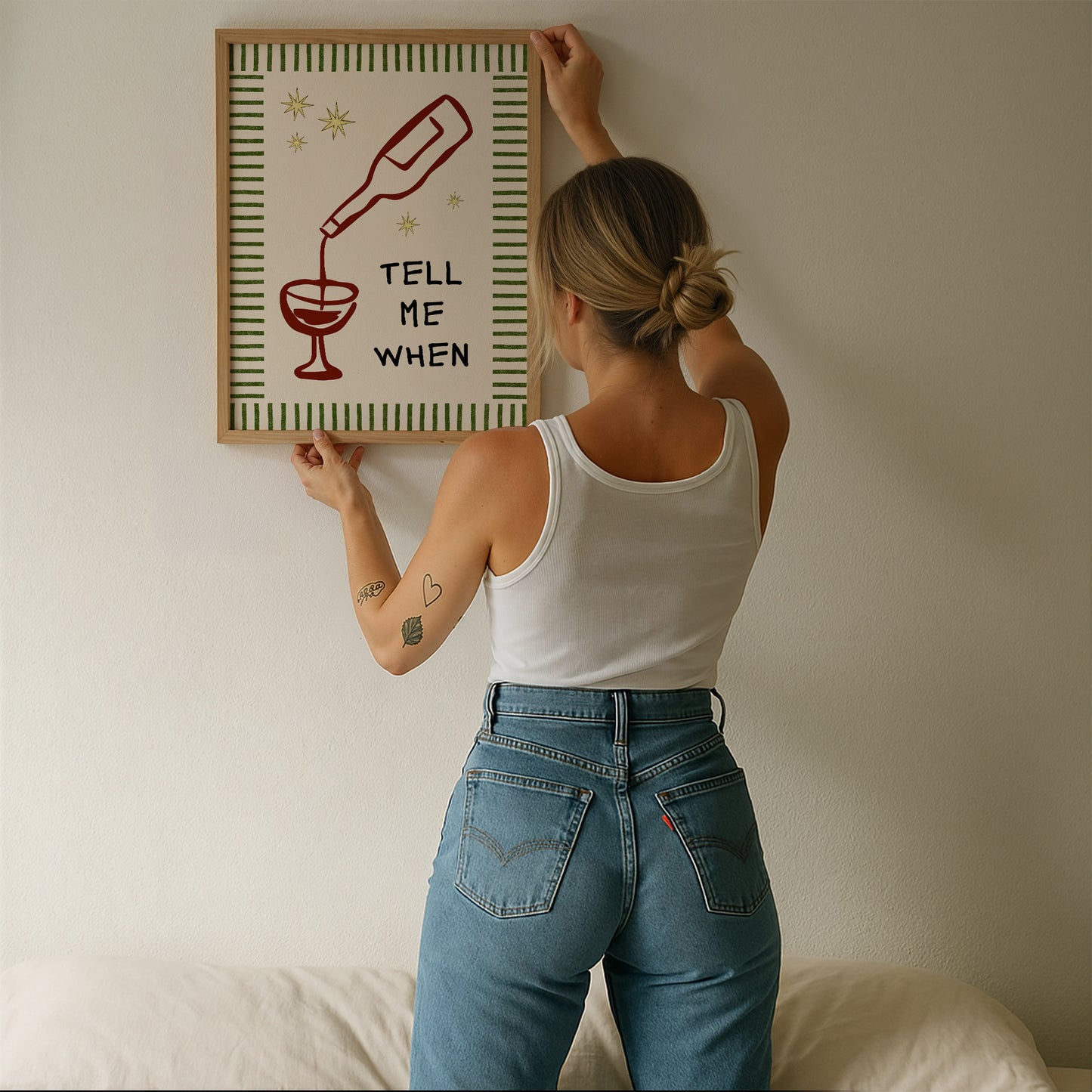 Vertical cream wall print with green stripe border, gold star details, and bold black typography reading Tell Me When alongside dark red hand-drawn line art of a wine bottle pouring into a glass
