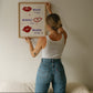 Cream print with three illustrated red lips paired with "Besos," "Bisous," and "Beijos" in navy lettering, with small red hearts scattered throughout