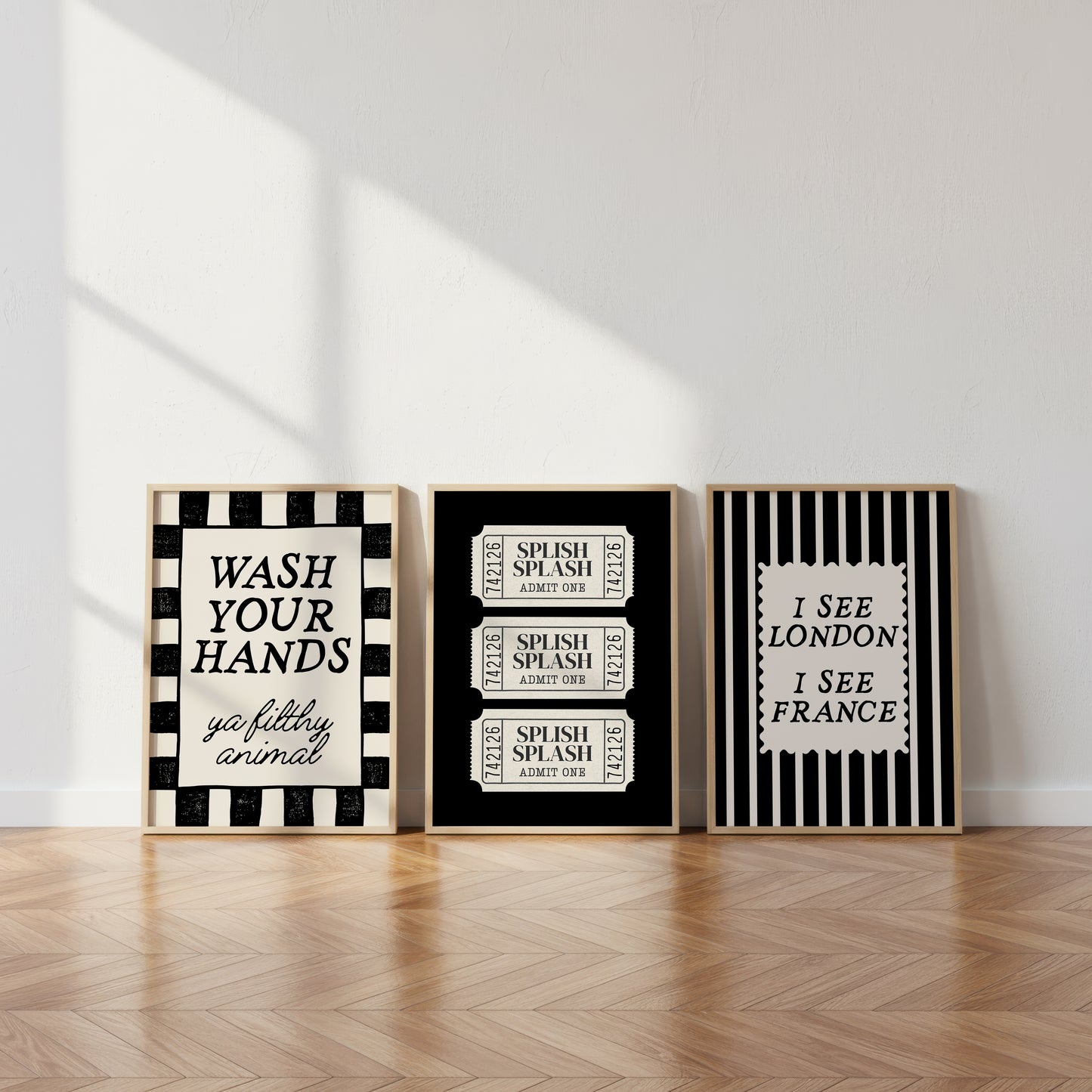 Set of 3 black and white bathroom prints: "Wash your hands ya filthy animal" in black cursive bordered by a black and white checkered frame, three black ticket-stub illustrations reading "Splish Splash, Admit One," and "I See London I See France" in a scalloped stamp frame on black and white stripes.