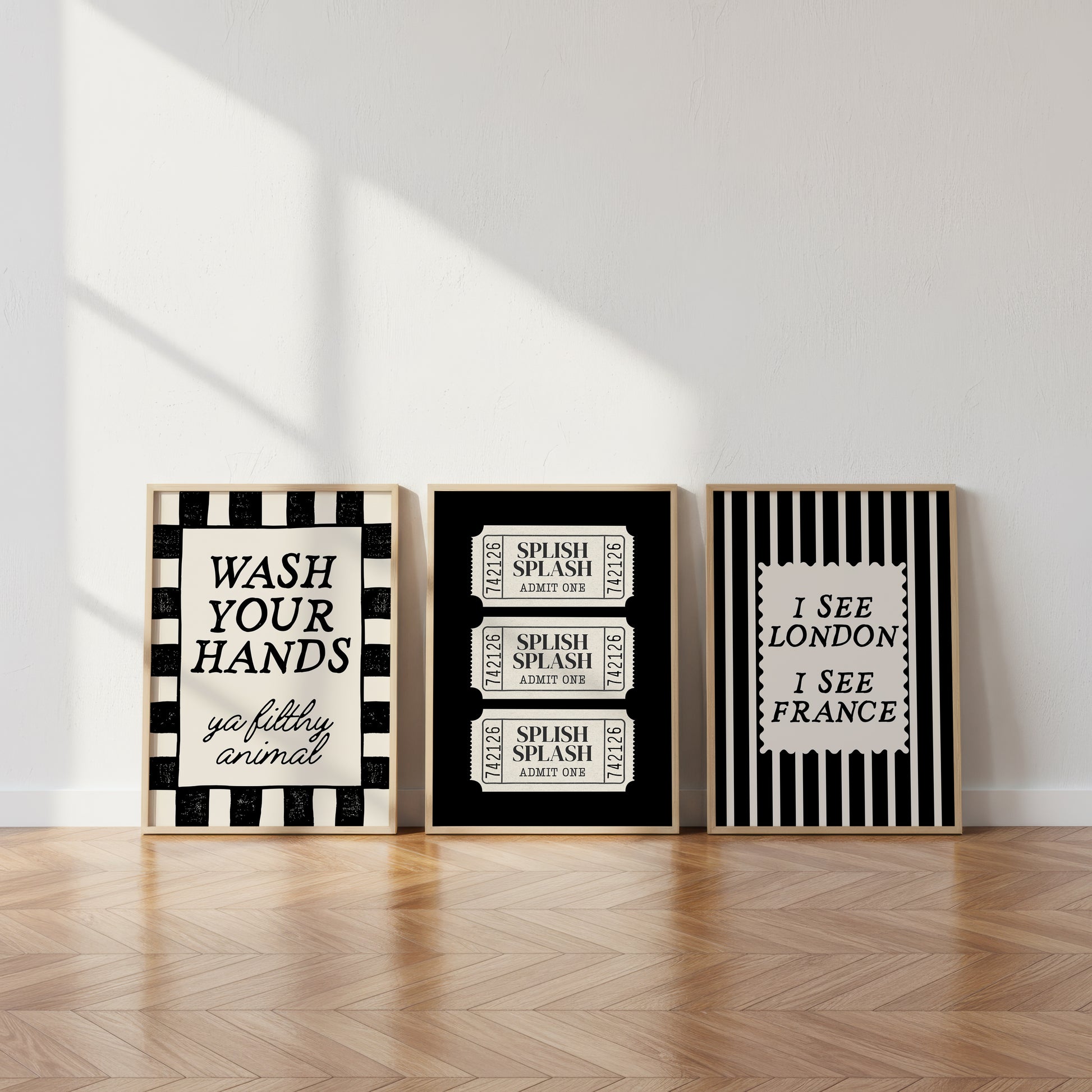Set of 3 black and white bathroom prints: "Wash your hands ya filthy animal" in black cursive bordered by a black and white checkered frame, three black ticket-stub illustrations reading "Splish Splash, Admit One," and "I See London I See France" in a scalloped stamp frame on black and white stripes.