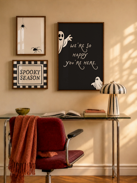 Set of 3 Halloween prints: a black background print with cartoon ghosts reading "We're so happy you're here," a checkered "Spooky Season" print, and a minimalist black spider illustration on a cream background.